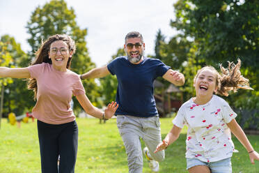 Carefree father with two daughters running on a meadow - MGIF00731