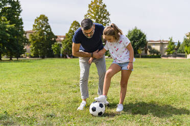 Vater und Tochter spielen Fußball auf einer Wiese - MGIF00732