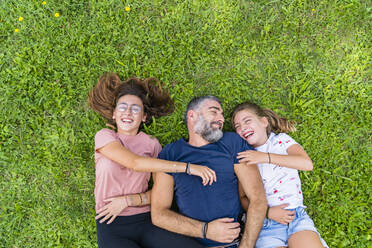 Happy father with two daughters lying on a meadow - MGIF00741