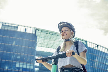 Portrait of smiling young woman with E-Scooter in the city, Berlin, Germany - BFRF02081