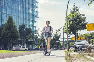 Junge Frau fährt E-Scooter auf dem Bürgersteig, Berlin, Deutschland - BFRF02083