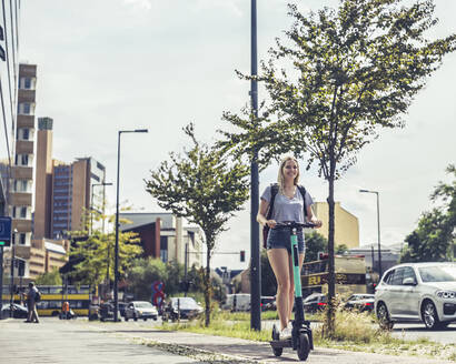 Lächelnde junge Frau fährt E-Scooter auf dem Fahrradweg, Berlin, Deutschland - BFRF02085