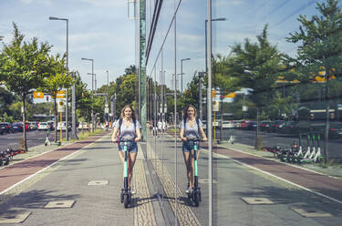 Junge Frau fährt E-Scooter auf dem Bürgersteig, Berlin, Deutschland - BFRF02086