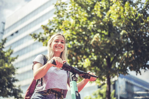 Porträt einer lächelnden jungen Frau mit einem E-Scooter, Berlin, Deutschland - BFRF02089