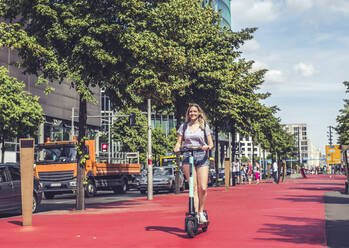 Young woman riding E-Scooter on Boulevard of the Stars, Berlin, Germany - BFRF02090