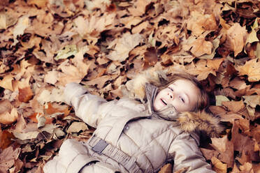 Mädchen liegt in einem Laubhaufen im Herbstwald - XCF00258