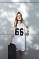Junge Frau trägt ein T-Shirt mit der Nummer 66 und hält ein Skateboard - JPTF00323