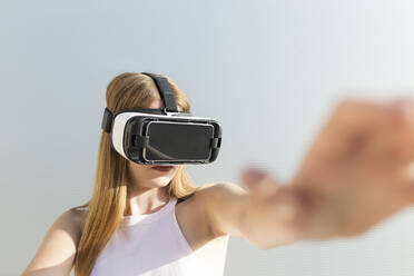 Young woman using Vr googles, reaching with her hand - JPTF00329