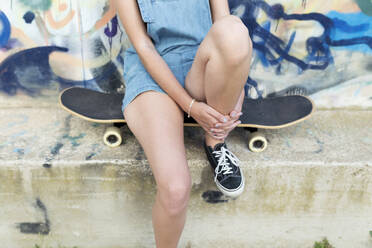 Junge Frau sitzt auf einem Skateboard vor einem Graffiti - JPTF00332