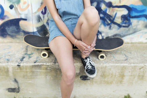 Junge Frau sitzt auf einem Skateboard vor einem Graffiti - JPTF00332