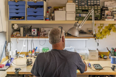 Ein älterer Mann arbeitet an elektronischen Schaltkreisen in seiner Werkstatt - AFVF04021