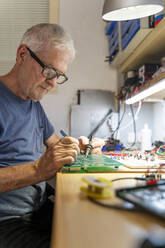 Senior man working on electronic circuits in his workshop - AFVF04023