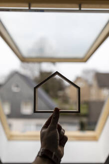 Hand hält Holzhausmodell gegen Fenster - GUSF02669