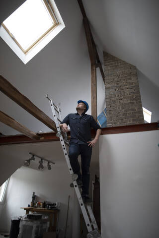 Architekt auf der Baustelle eines Dachgeschossausbaus, auf der Leiter stehend, lizenzfreies Stockfoto