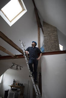 Architekt auf der Baustelle eines Dachgeschossausbaus, auf der Leiter stehend - GUSF02680