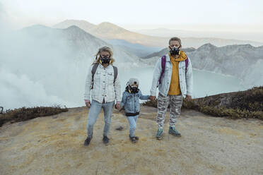 Familie mit Atemschutzmasken steht Hand in Hand am Rande des Vulkans Ijen, Java, Indonesien - KNTF03617