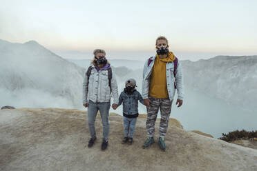 Familie mit Atemschutzmasken steht Hand in Hand am Rande des Vulkans Ijen, Java, Indonesien - KNTF03618