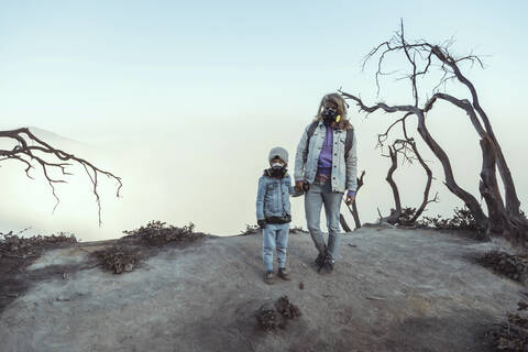 Mutter und Sohn mit Atemschutzmasken stehen Hand in Hand am Rande des Vulkans Ijen, Java, Indonesien, lizenzfreies Stockfoto