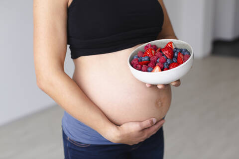 Junge schwangere Frau isst verschiedene Arten von frischem Obst, lizenzfreies Stockfoto