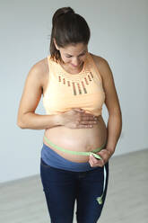 Junge schwangere Frau misst ihren Babybauch - HMEF00598