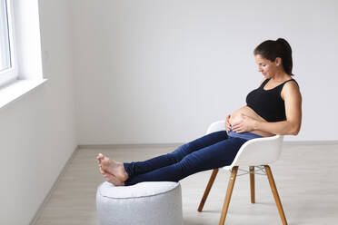 Junge schwangere Frau sitzt auf einem Stuhl und denkt über die Zukunft nach - HMEF00599