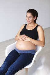 Young pregnant woman sitting on chair and is thinking about the future - HMEF00600