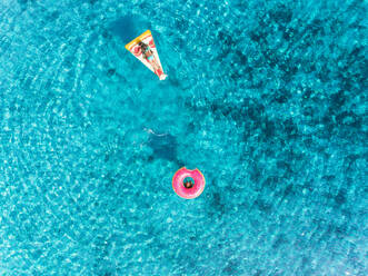 Luftaufnahme von zwei jungen Mädchen, die im Meer schwimmen und mit aufblasbaren Pizzen und Donuts spielen. - AAEF03666