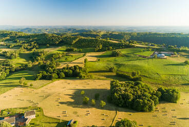 Luftaufnahme von langschattigen Hügeln und Strohballen auf einem Feld in Correze, Frankreich. - AAEF03702