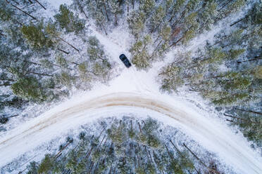 Luftaufnahme eines Autos, das im Schnee im Wald von Estland fährt. - AAEF04040