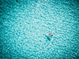 Luftaufnahme einer Frau im Bikini, die im transparenten türkisfarbenen tropischen Meerwasser schwimmt - AAEF04125
