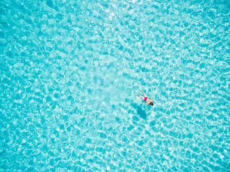 Luftaufnahme einer Frau im Bikini, die im transparenten türkisfarbenen tropischen Meerwasser schwimmt - AAEF04126