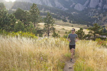 Mann läuft durch hohes Gras auf dem Bear Canyon Trail in Boulder, Colorado - CAVF63391