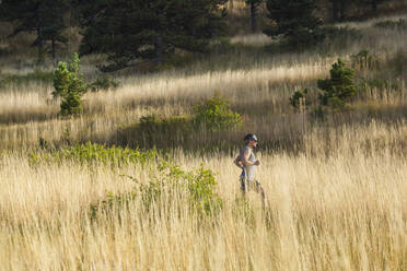 Man runs through tall grass in Bear Canyon above Boulder, Colorado - CAVF63393