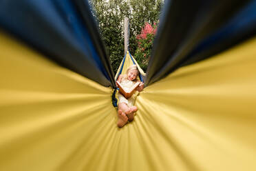 Happy tween girl reading in a yellow hammock - CAVF63470