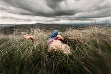 Young boy lying in tall grass - CAVF63478