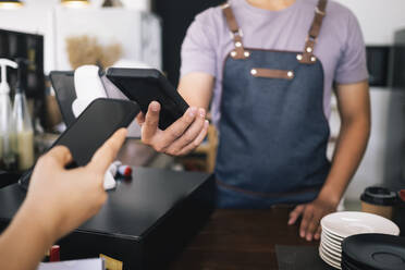 Kunde beim kontaktlosen Bezahlen mit dem Telefon in einem Café. - CAVF63523