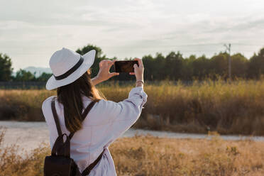 Junge Frau fotografiert mit ihrem Smartphone auf einem Feld. Abenteuer, Technik - CAVF63561