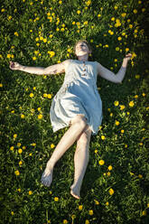 Young woman lying down in dandelion field in early spring. - CAVF63641