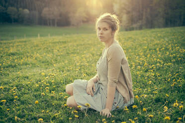Young woman sitting in dandelion field in early spring. - CAVF63643