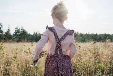 Rückansicht eines jungen Mädchens, das mit Wildblumen in der Hand über eine Wiese läuft - CAVF63666