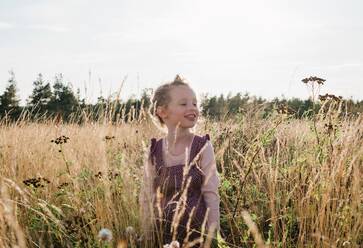 Porträt eines jungen Mädchens, das lächelnd auf einer Wiese mit wilden Blumen sitzt - CAVF63669