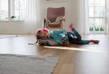 Young girl laying on the floor with headphones on listening to music - CAVF63671