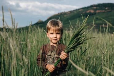 Junge mit ernstem Gesichtsausdruck, der Gras hält - CAVF63675