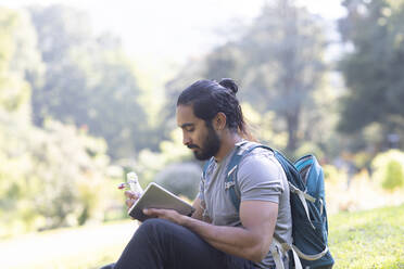 Junger Wanderer in Indien entspannt sich mit Tablet und Flasche in den Händen - CAVF63695