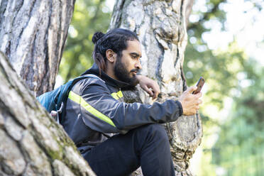 Junger Wanderer in Indien sitzt und überprüft sein Smartphone - CAVF63701