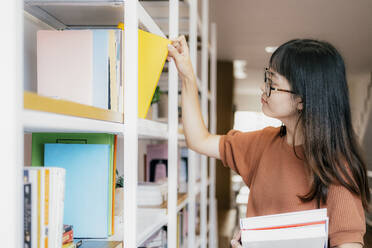 Junger Teenager, der in einer Buchhandlung eine Bestellung in den Bücherregalen aufgibt. - CAVF63724