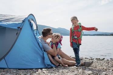 Ein Vater küsst seine Tochter, während seine Familie beim Camping am Meer spielt - CAVF63877