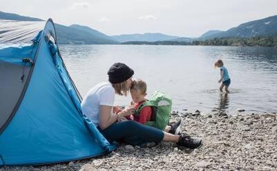 Mutter küsst ihren Sohn, während sie mit ihrer Familie in einem Zelt am Meer zeltet - CAVF63878