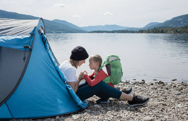 Mutter hält Söhne Hände und lächelnd saß in einem Zelt Camping am Meer - CAVF63879