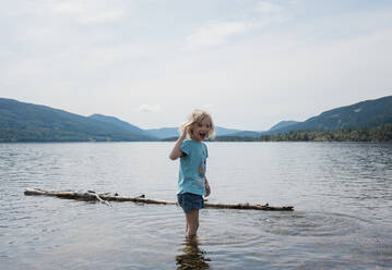Junges Mädchen lächelnd im Wasser stehend, umgeben von Bergen - CAVF63880